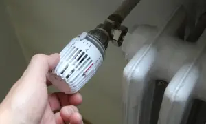 Mano che regola la manopola del termosifone, scegliendo tra senso orario o antiorario per la temperatura desiderata.