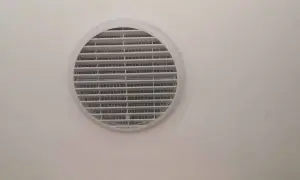 Foro ventilazione cucina entra freddo. La griglia bianca circolare è montata su una parete chiara.