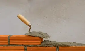 Cazzuola con malta a base di calce pronta per posare un mattone su una parete in costruzione.