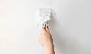 Mano con spatola che rimuove carta da parati bianca da un muro.
