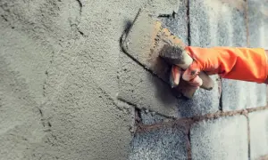 Mano con guanto arancione stende malta per stuccare muri in pietra con una cazzuola.