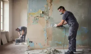 Operai al lavoro per rimuovere vecchi strati di pittura e preparare il muro per un nuovo intonaco rasato.