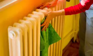 Mani che puliscono un termosifone in ghisa con un panno verde. Il lavaggio interno termosifoni in ghisa è importante per l'efficienza.