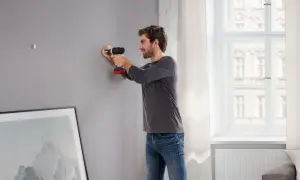 Uomo usa trapano per fissare listelli di legno al muro, preparando la parete per appendere un quadro.