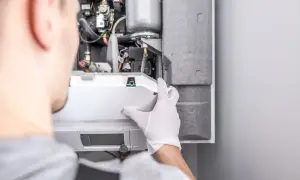 Tecnico con guanti bianchi effettua la revisione della caldaia, controllando i componenti interni.