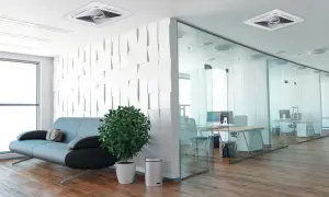 Un moderno ufficio con un divano, una pianta e un condizionatore incassato nel controsoffitto. La zona lavoro è separata da pareti in vetro.