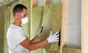 Operaio con mascherina e occhiali installa pannelli di lana di roccia per un cappotto termoisolante.