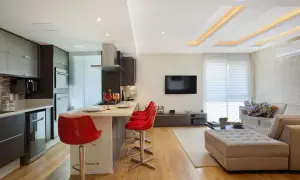 Elegante cucina moderna con isola e sgabelli rossi, separata dal soggiorno da un pratico cartongesso divisorio.