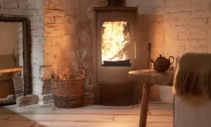 Un accogliente impianto riscaldamento a legna con fiamme vive, cesto di legna e teiera su un tavolino rustico.