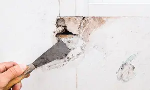 Mano con spatola che prepara un grosso buco nel muro per come riempire il muro danneggiato.