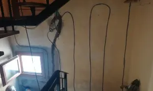 Lavori in corso per l'isolamento pilastri: cavi neri corrono lungo la parete accanto a una scala e una finestra.