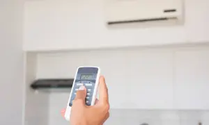 Mano che regola il telecomando del condizionatore in modalità "DRY" per un clima più asciutto.