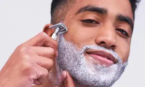 Uomo con schiuma da barba aggrappante prima della rasatura, mentre usa un rasoio di sicurezza.