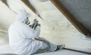 Operaio in tuta protettiva applica schiuma espansa per un efficace isolamento termico del sottotetto.