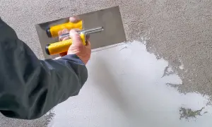 Mano con spatola gialla applica pittura rasante su muro grezzo, creando una superficie liscia e uniforme.