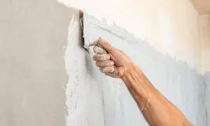 Mano che applica intonaco spugnato su una parete con una spatola. La texture è grezza e irregolare.