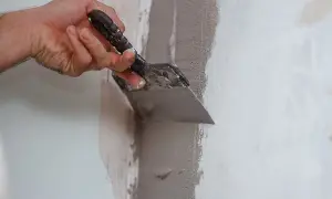 Mano che stende premiscelato per chiudere tracce su un muro con una spatola.