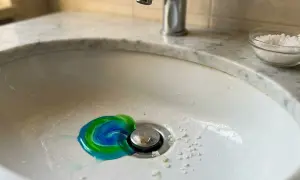 Un lavandino con un vortice di sapone blu e verde vicino allo scarico, e del sale grosso per sturare lavandini sparso sul bordo.