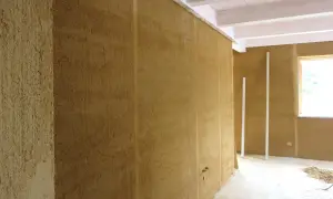 Interno di una stanza con pareti in **mattone crudo** grezzo, travi a vista e una finestra.