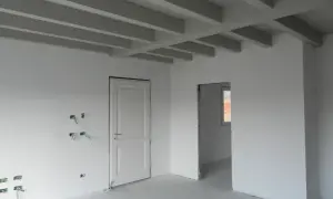 Interno in fase di finitura: pareti bianche, travi a vista e predisposizioni elettriche. Lo spessore intonaco interno è uniforme.