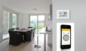 Termostato e cronotermostato: un confronto visivo. Un moderno soggiorno con tavolo da pranzo e un dispositivo di controllo della temperatura, accanto a uno smartphone che mostra un'app per la gestione della casa.