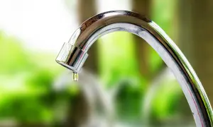Close-up of a dripping chrome faucet with a water droplet forming.