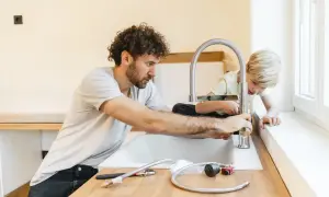 Padre e figlio installano un nuovo rubinetto in cucina, un'operazione che richiede attenzione per spostare attacchi cucina senza rompere pavimento.