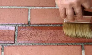 Mano con pennello applica prodotto per restauro mattoni faccia a vista, rinnovando la parete.