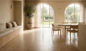 Luminoso soggiorno con pavimento in pastellone veneziano, divanetto imbottito, ulivo in vaso e ampie finestre ad arco che si affacciano sul giardino.