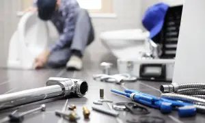 Idraulico al lavoro su un water, con attrezzi e tubi in primo piano. La pendenza scarico cucina è fondamentale per un corretto deflusso.