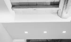 Soffitto con faretti incassati e travi a vista. Una moderna colonna cartongesso con nicchie illumina l'ambiente.