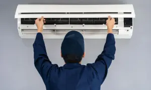 Tecnico con cappellino blu apre il pannello di un condizionatore per manutenzione.