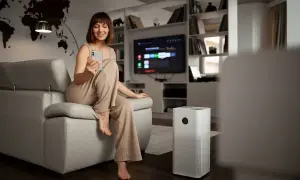 Donna sorride usando il telefono, accanto a un purificatore d'aria che garantisce la funzione deumidificatore.