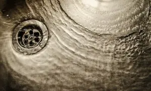 Acqua che scorre su uno scarico metallico, un'immagine che evoca il processo di come sciogliere il grasso nei tubi di scarico.