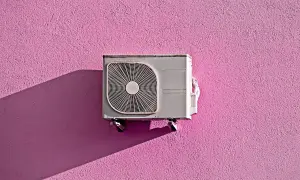 Unità esterna di condizionatore appesa a un muro rosa acceso, con ombra proiettata. Pensando allo smaltimento condizionatori.