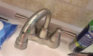 Rubinetti del bagno con calcare verde incrostato. Accanto, salviettine e una bomboletta di schiuma da barba.