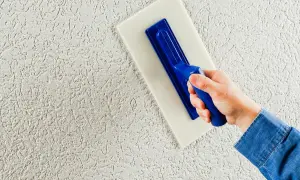 Mano che applica intonaco esterno con frattazzo, creando una texture rustica. Lo spessore intonaco esterno è visibile.