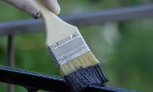 Mano guantata che inizia a verniciare ringhiera con pennello nero.