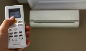 Mano che regola il telecomando del condizionatore, impostando la temperatura. Scopri quanto consuma un condizionatore per un comfort ottimale.