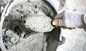 Mano guantata raccoglie cemento fresco da un secchio. I materiali leganti sono pronti per l'uso.