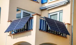 Due pannelli solari da balcone catturano l'energia del sole, montati su una ringhiera con tende a righe blu e bianche.