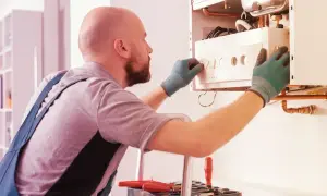 Tecnico con guanti verdi effettua la revisione caldaia in ritardo, regolando i comandi.