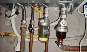 Manutenzione caldaia: pulizia filtro defangatore. Si vedono tubi, valvole e due filtri, uno con liquido giallo e uno con liquido scuro.