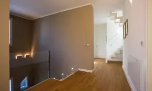 Un moderno disimpegno casa con scala bianca a vista, parapetto in vetro e luci a led che illuminano il corridoio.