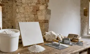 Attrezzi da muratore e secchio di calce idraulica su un tavolo di legno, pronti per il restauro di un muro in pietra.