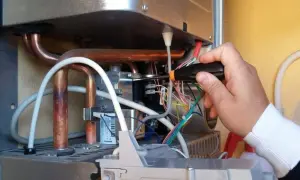 Tecnico effettua la pulizia della caldaia, lavorando sui cablaggi interni con un cacciavite.