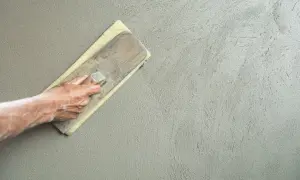 Mano che stende l'intonaco con una spatola, creando una finitura liscia. La rasatura 5 mm è quasi completa.