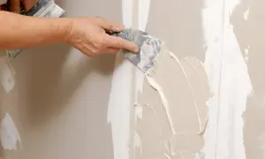 Mano stende stucco su una giuntura di cartongesso, ricordando che il cartongesso ha un verso.
