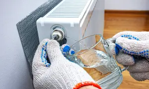 Mani guantate raccolgono acqua da un bicchiere mentre si impara come sfiatare i termosifoni, liberando l'aria intrappolata.