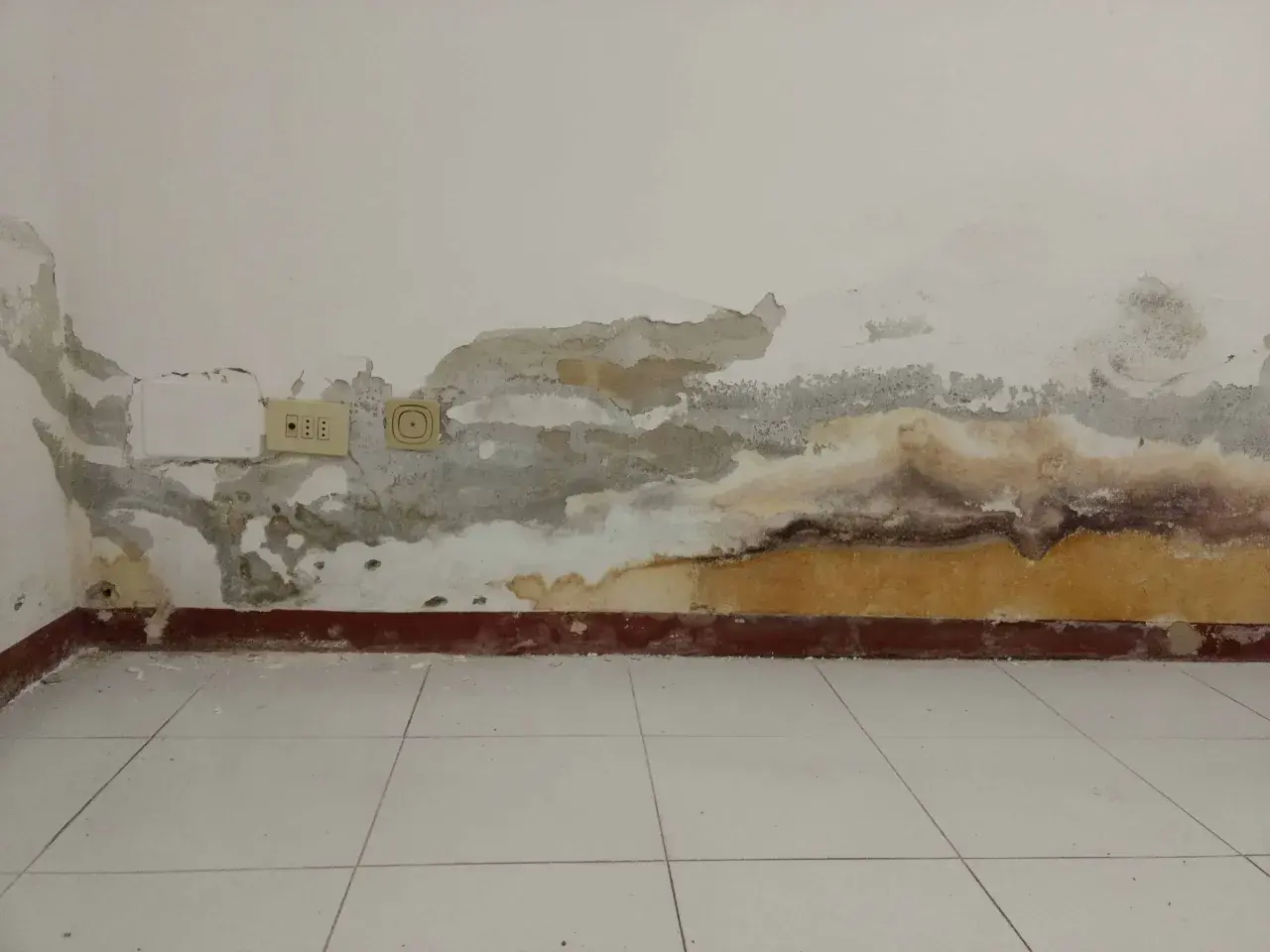Muri con intonaco antiumido scrostato e macchie di umidità, prese elettriche visibili.
